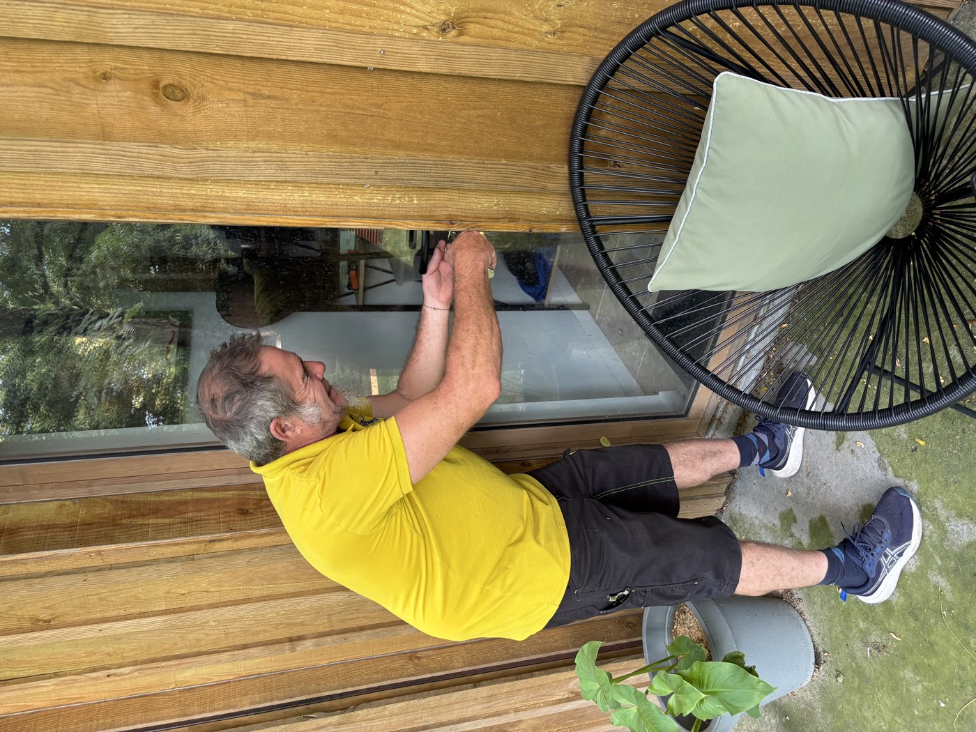Michel dépanne la serrure de la porte vitrée d'un studio de jardin en bois